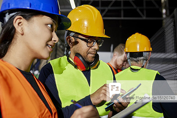 Male and female worker with clipboard and tablet talking in factory