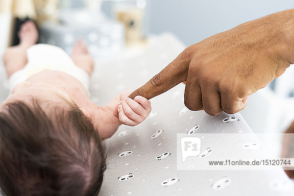 Nahaufnahme eines Neugeborenen  der den Finger des Vaters auf dem Wickeltisch ergreift