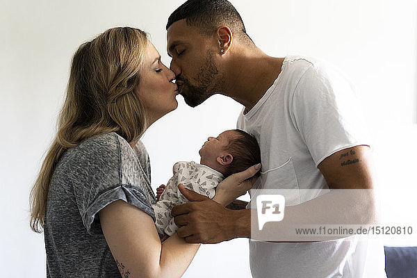 Küssende Eltern  die ihr Neugeborenes zu Hause halten