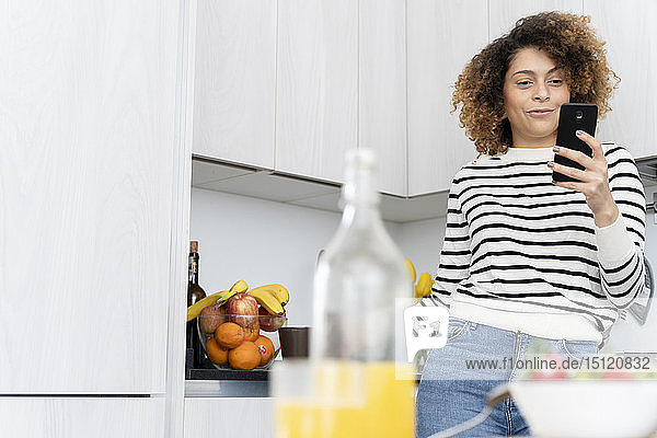 Woman standing in kitchen using smartphone