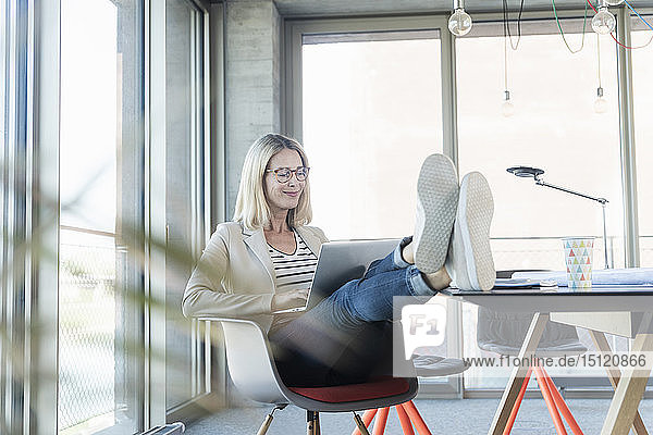 Relaxed businesswoman using laptop in office with feet up
