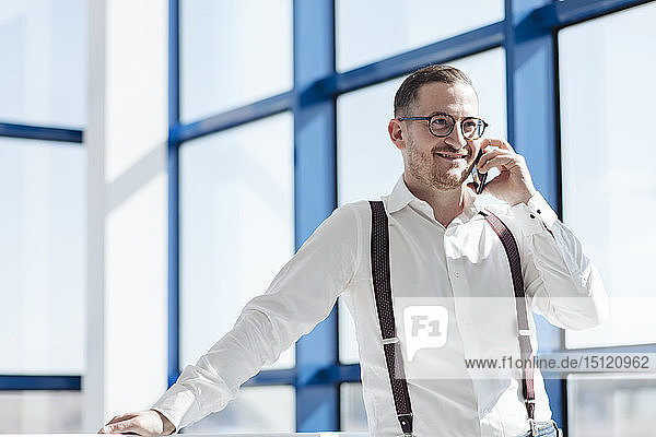 Smiling businessman talking on cell phone at the window in modern office