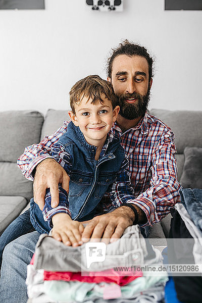 Porträt von Vater und Sohn  die zusammen auf der Couch sitzen und Wäsche zusammenlegen