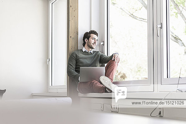 Young businessman sitting on windowsill  using laptop