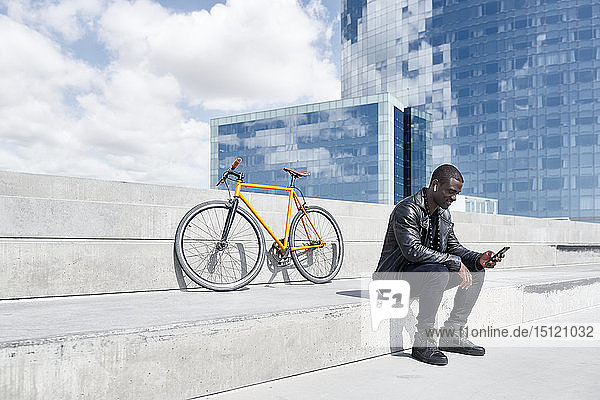Mann mit gelbem Fahrrad sitzt auf einer Treppe und benutzt ein Smartphone  Barcelona  Spanien