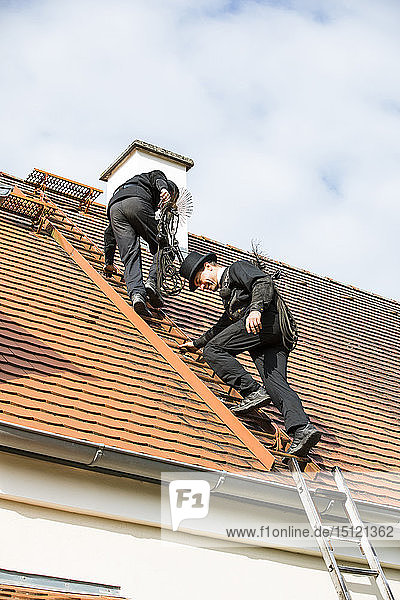 Zwei Schornsteinfeger klettern auf Hausdach