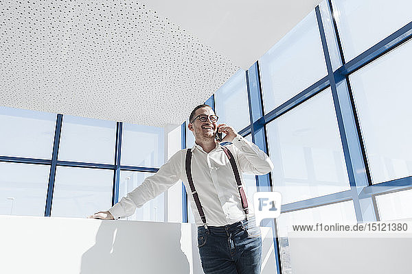 Happy businessman talking on cell phone at the window in modern office