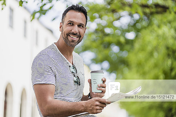 Lächelnder Mann mit Kaffee zum Mitnehmen und Zeitung in einem Park