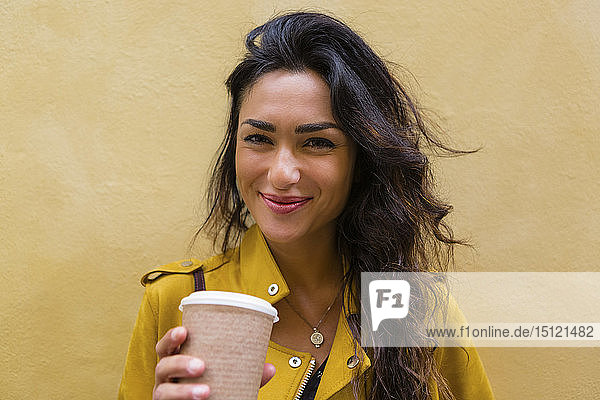 Porträt einer jungen Frau in gelber Lederjacke  die eine Tasse Kaffee hält