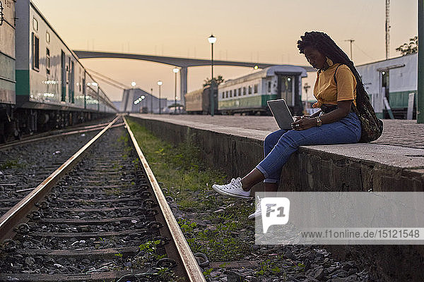 Junge Frau sitzt auf dem Bahnsteig im Bahnhof mit Laptop