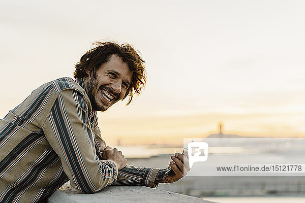 Portrait of laughing man with smartphone during sunset  Barcelona  Spain