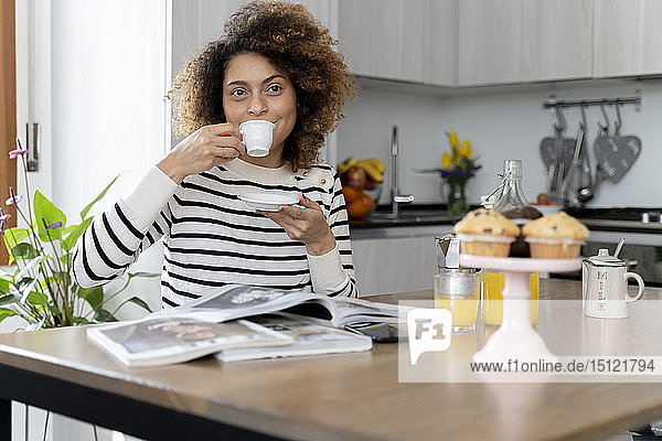 Frau sitzt in der Küche  liest Zeitschriften und trinkt Kaffee