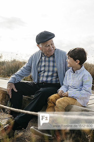 Großvater sitzt mit seinem Enkel an der Strandpromenade und sieht einander an