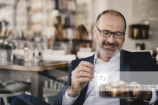 Ein reifer Geschäftsmann mit einem Stück Kuchen auf einem digitalen Tablet in einem Cafe