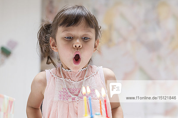 Portrait of little girl blowing out burning candles on her birthday cake