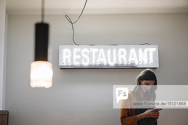 Young woman using cell phone under restaurant neon light