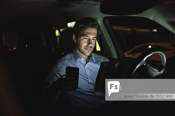 Junger Mann benutzt nachts im Auto Handy und Tablet