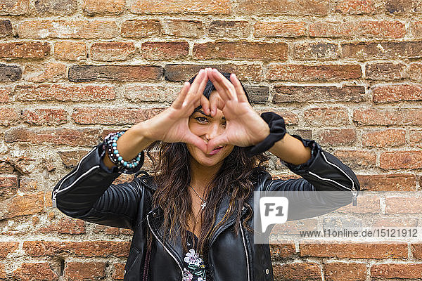 Portrait of young making heart shape with hands and fingers  brick wall