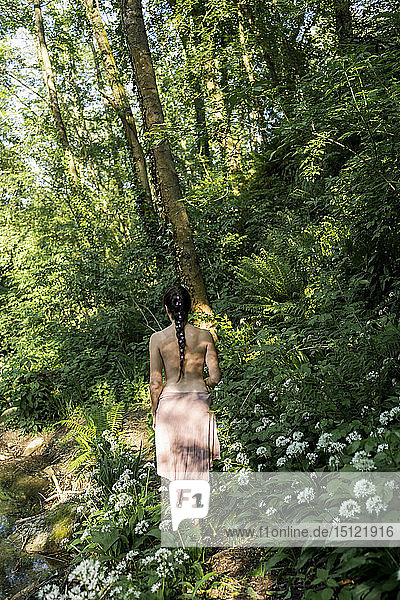 Rückansicht einer barbusigen jungen Frau  die in einem üppigen Wald spazieren geht  Garrotxa  Spanien