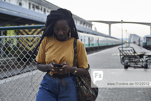 Junge Frau auf dem Bahnsteig am Bahnhof überprüft ihr Telefon