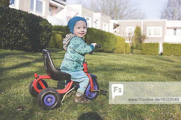 Porträt eines glücklichen kleinen Jungen mit Dreirad auf dem Rasen