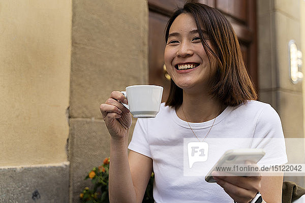 Italien  Florenz  glückliche junge Frau mit Handy in einem Café im Freien