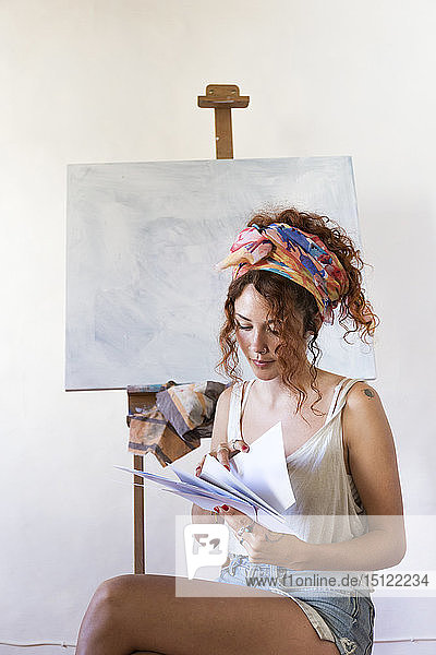 Junge Malerin im Kunstatelier neben leerer Leinwand beim Betrachten von Papier