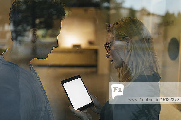 Junger Mann und Frau teilen sich ein Tablett hinter einer Fensterscheibe