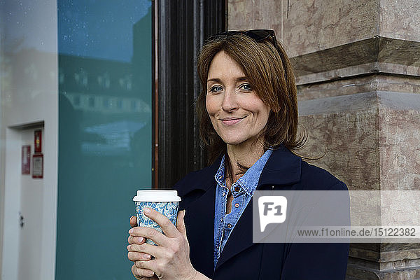 Portrait of smiling mature woman with reusable bamboo cup in the city