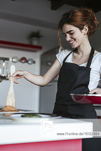 Lächelnde junge Frau legt in ihrer Küche Fritten auf Pastete
