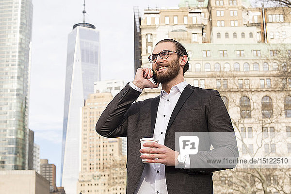 Smiling young businessman with coffee to go on the phone  New York City  USA