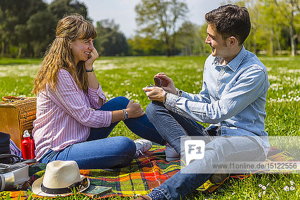 Junger Mann macht seiner Freundin in einem Park einen Heiratsantrag