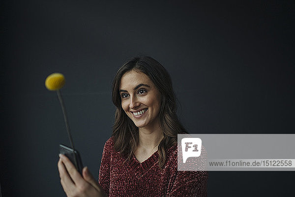 Smiling young woman using flower as antenna for cell phone