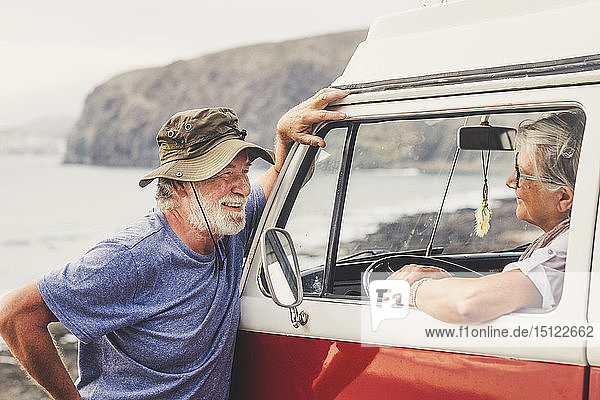 Älteres Ehepaar reist in einem Oldtimer-Van  macht eine Pause am Meer  unterhält