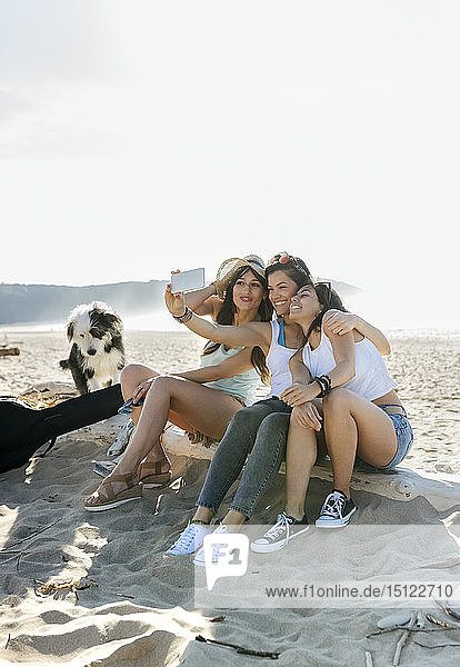 Glückliche Freundinnen mit Hund  die am Strand ein Selfie machen