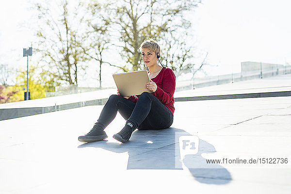 Porträt eines jungen Freiberuflers  der mit digitalem Tablett und Headset im Freien sitzt