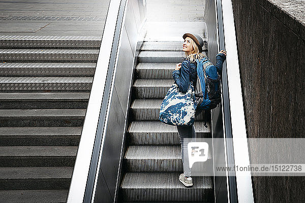Woman with backpack and travelling bag standing on escalator looking up