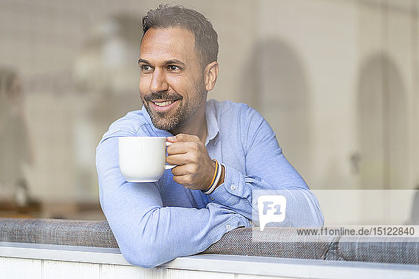 Lächelnder Geschäftsmann mit einer Tasse Kaffee  der aus dem Fenster schaut