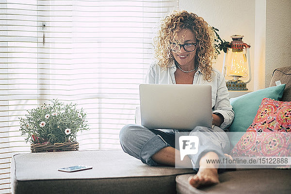 Lächelnde Frau mit Laptop auf der Couch zu Hause