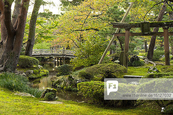 Hanambashi Bridge and a stone gate surrounded by autumn foliage in the Kenrokuen Garden Kanazawa Ishigawa Japan Asia