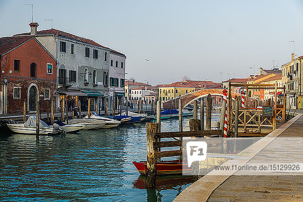 View of Ponte San Martino stone bridge over canal with colorful buildings and moored boats on wooden wharf pilings  Murano  Venice  UNESCO World Heritage Site  Veneto  Italy  Europe