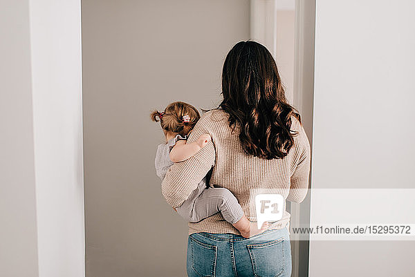 Mother carrying baby daughter through hall doorway  rear view
