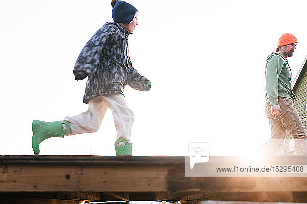 Junge mit Vater läuft über die sonnenbeschienene Skateboard-Rampe Blickwinkel niedrig