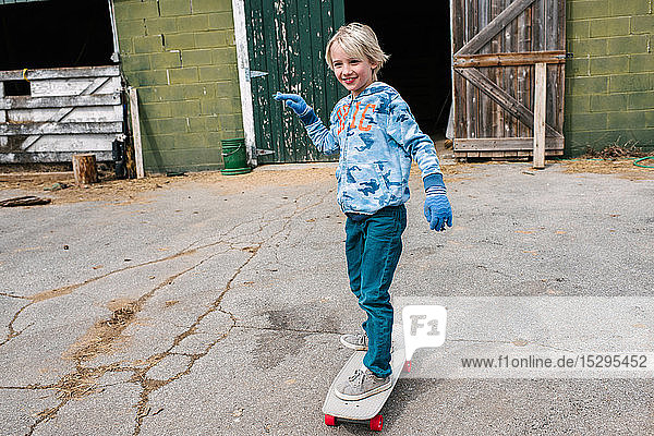 Blonder Junge fährt Skateboard auf dem Bauernhof
