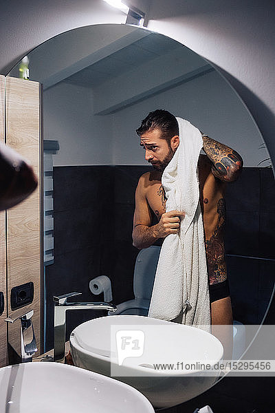 Mittelgroßer erwachsener Mann mit Tätowierungen  die Haare am Badezimmerspiegel trocknen  Spiegelbild