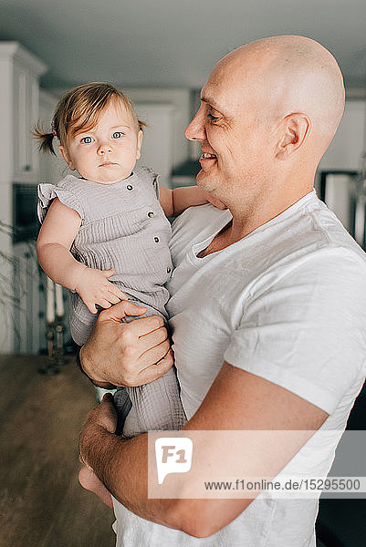 Father carrying baby daughter in living room  portrait