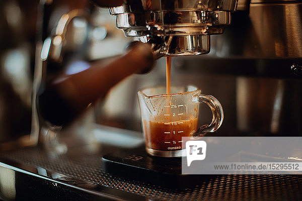 Barista gießt frischen Kaffee in Messbecher auf Kaffeemaschine im Café  flacher Fokus