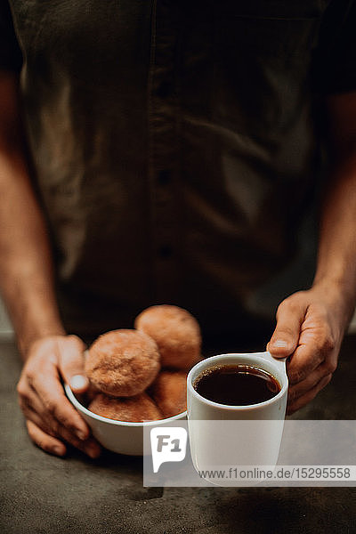 Barista platziert schwarzen Kaffee und Doughnuts auf Café-Theke  abgeschnittener flacher Fokus
