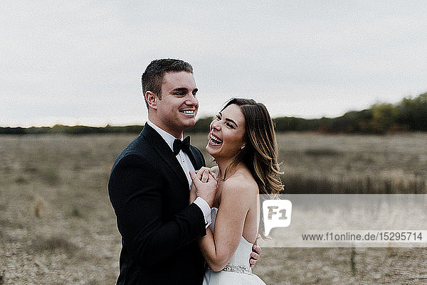 Happy young bride and groom hugging and laughing in field