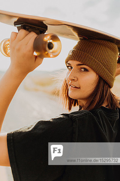 Junge Frau mit Skateboard auf dem Kopf auf einer Landstrasse  Portrait  Exeter  Kalifornien  USA